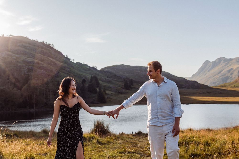 Scenic mountain landscape with couple walking hand in hand through grassy meadow against dramatic mountain backdrop.