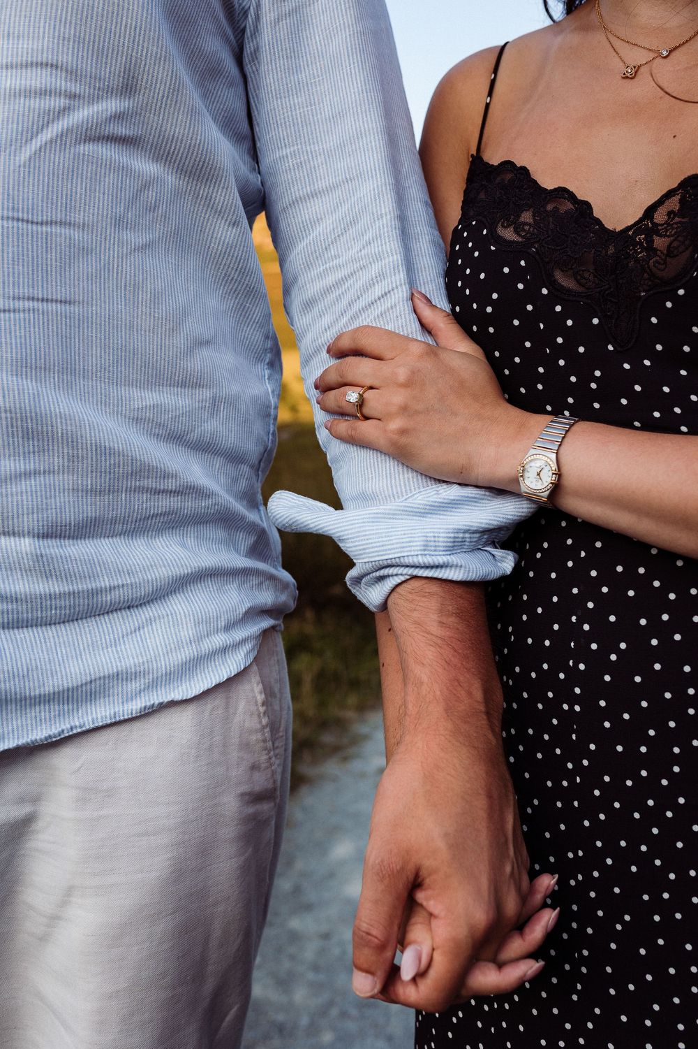 A couple holding hands wearing a blue button-down shirt and black polka dot dress with lace details.