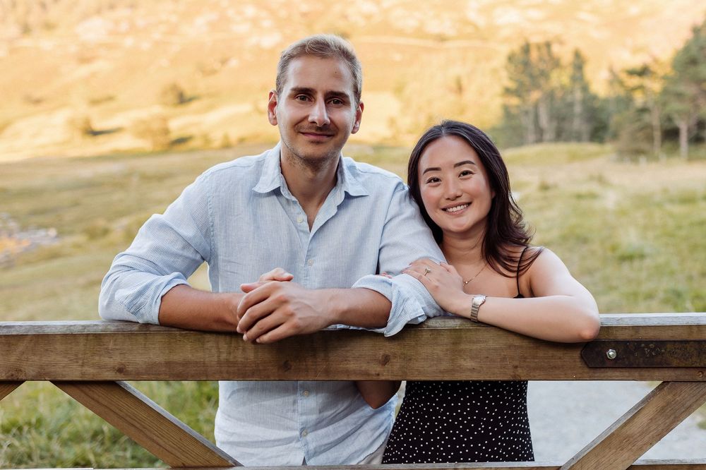 Couple shares intimate moments along a wooden fence with scenic mountain views at dusk.
