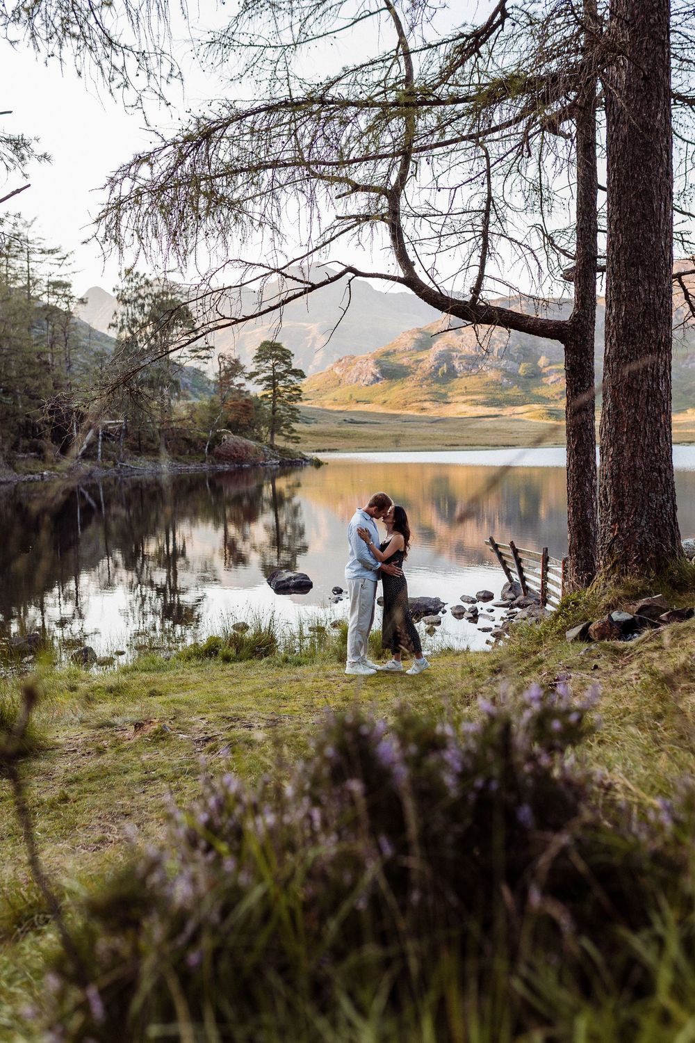 Tranquil lakeside scene with tall pine trees framing a couple sitting by the water.