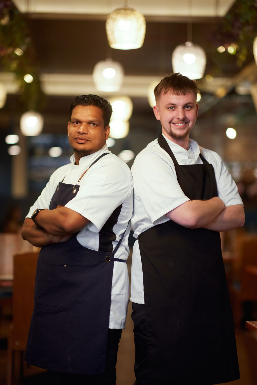 Restaurant staff in white shirts and dark aprons posing together in a warmly lit dining room.