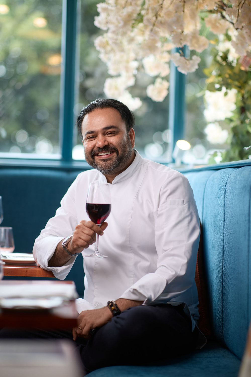 Person in chef whites relaxing on blue restaurant seating while enjoying a glass of wine.