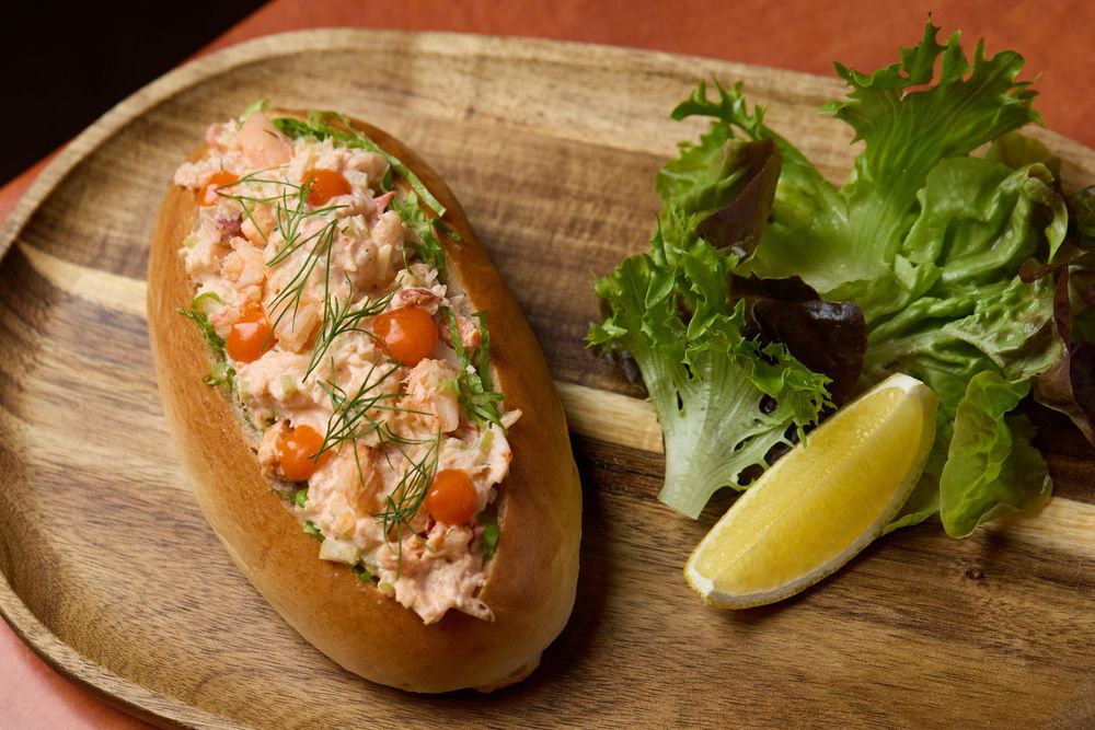 Fresh lobster rolls garnished with herbs and lemon wedges served on wooden boards.