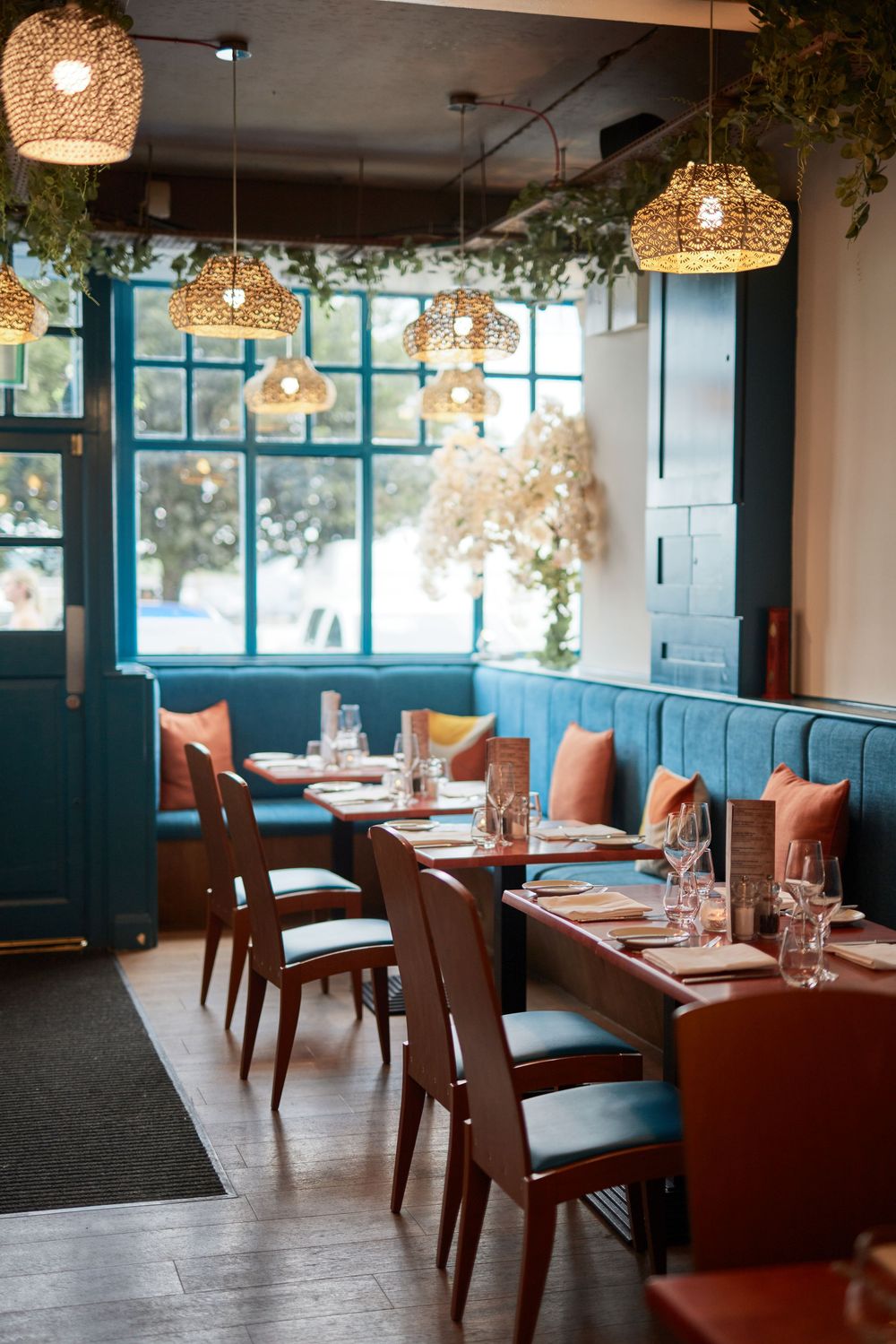 Modern restaurant dining room with brown leather seating and pendant lighting.