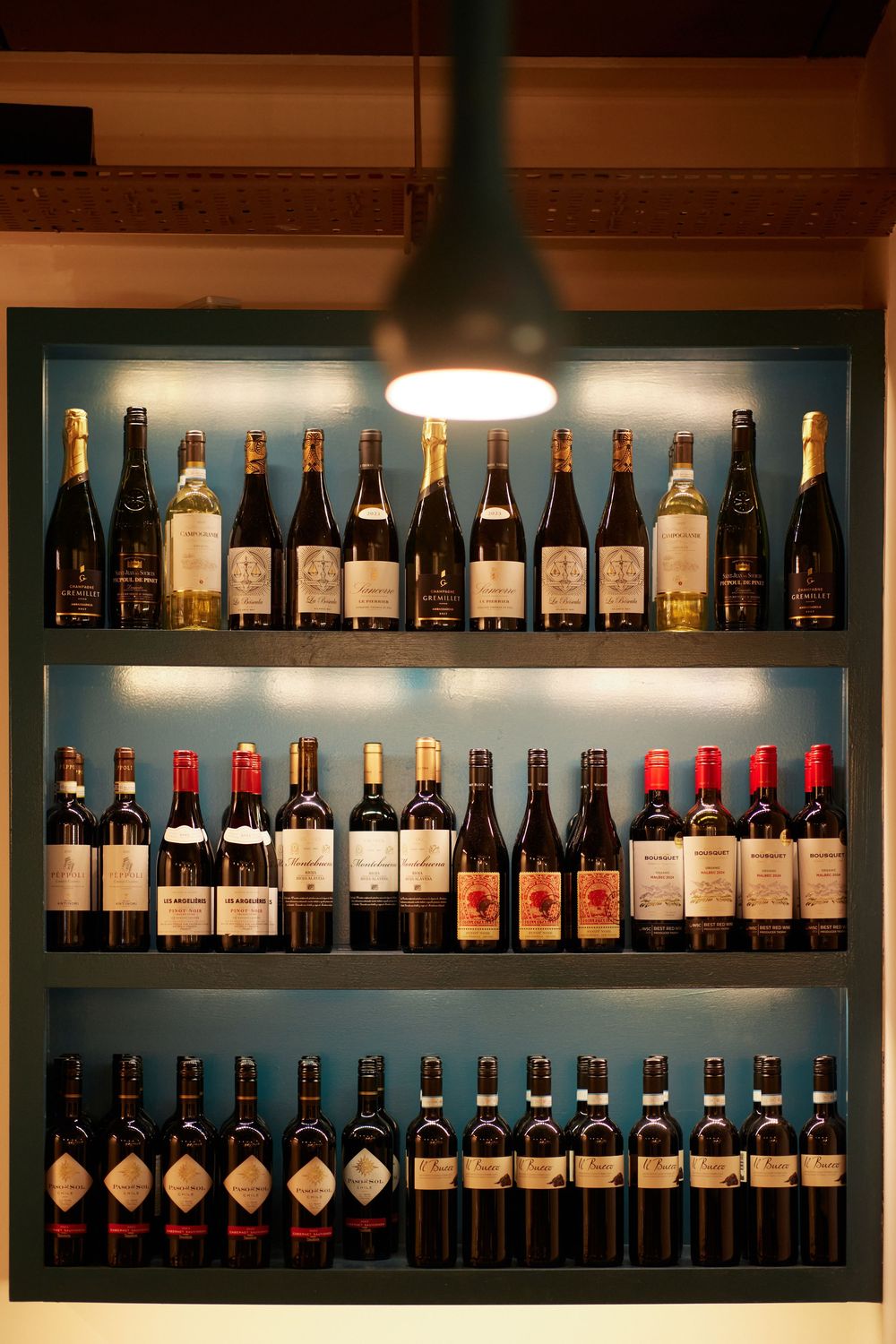 Illuminated wall display of wine bottles arranged on modern shelving.
