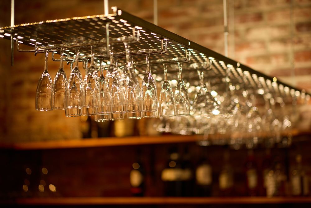 Row of hanging wine glasses illuminated above restaurant bar.