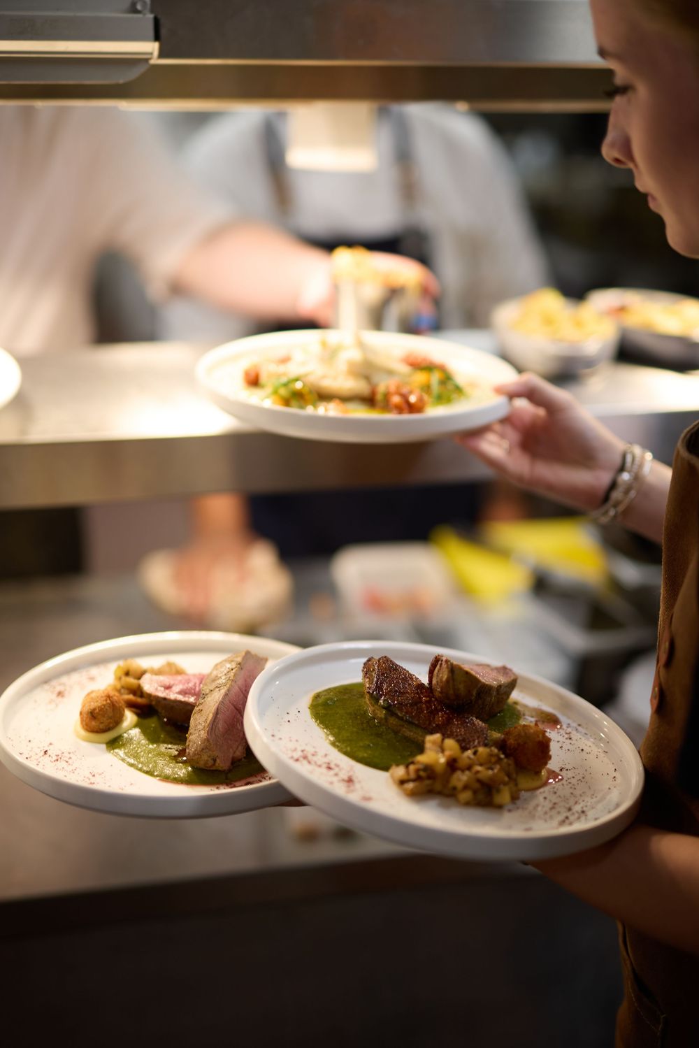 Multiple plates of elegantly plated meat dishes being served in a restaurant kitchen.