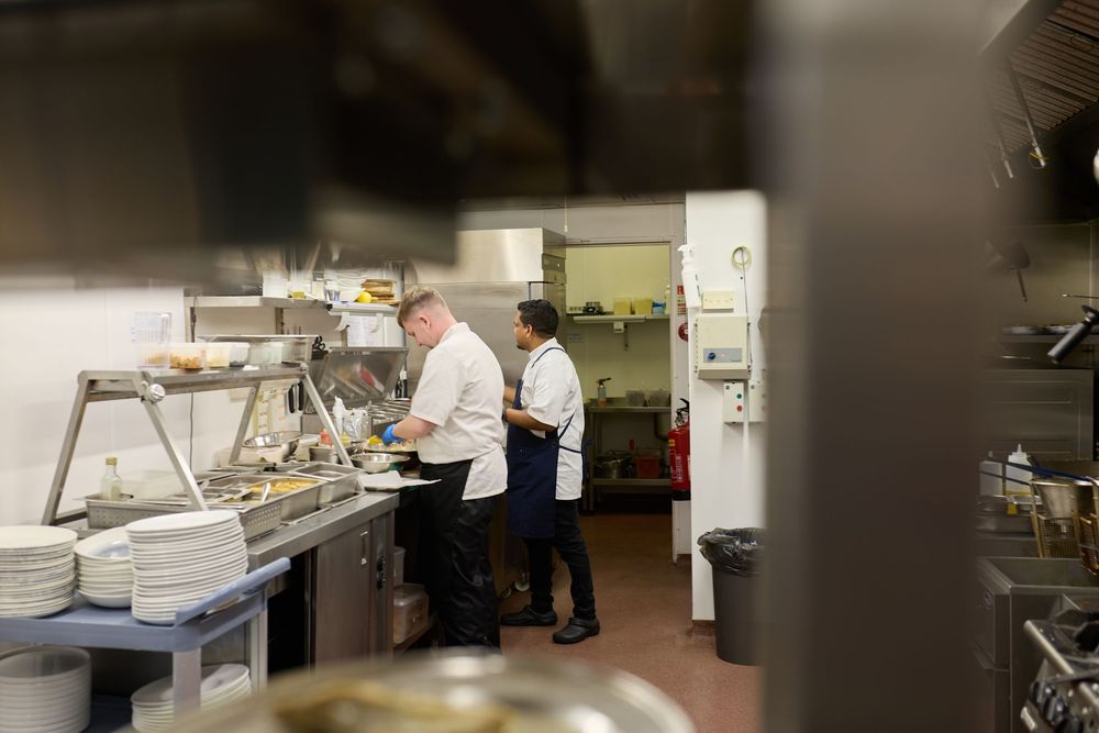 Interior view of a commercial kitchen with stainless steel equipment and staff working in the background.
