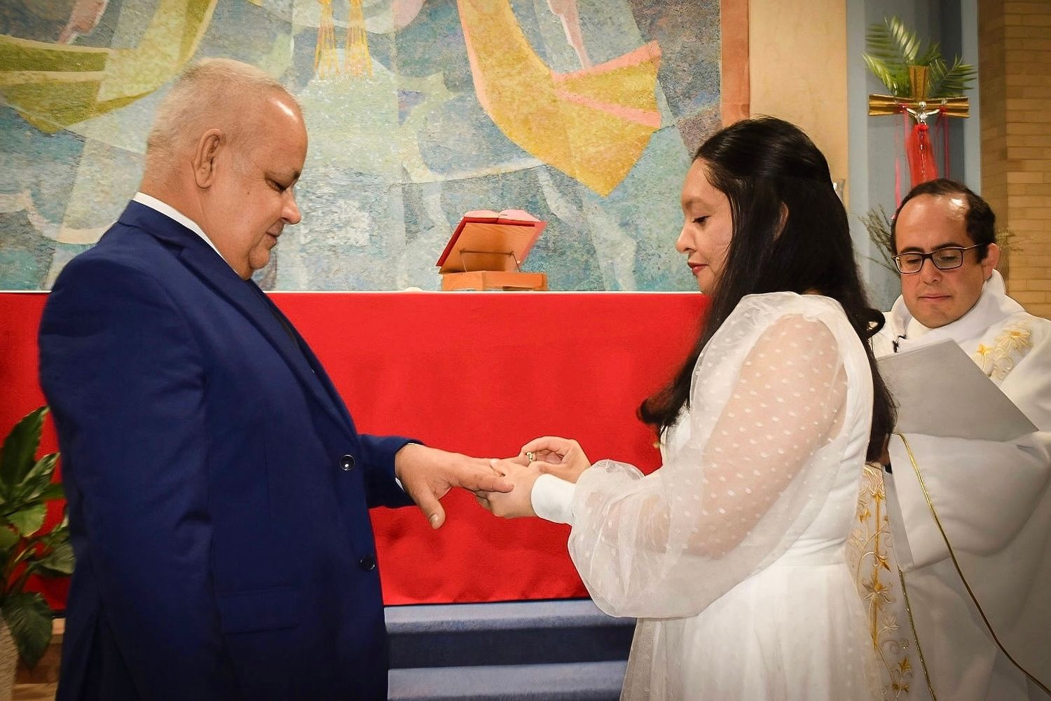 A couple shares a tender moment during their wedding ceremony in front of religious artwork.