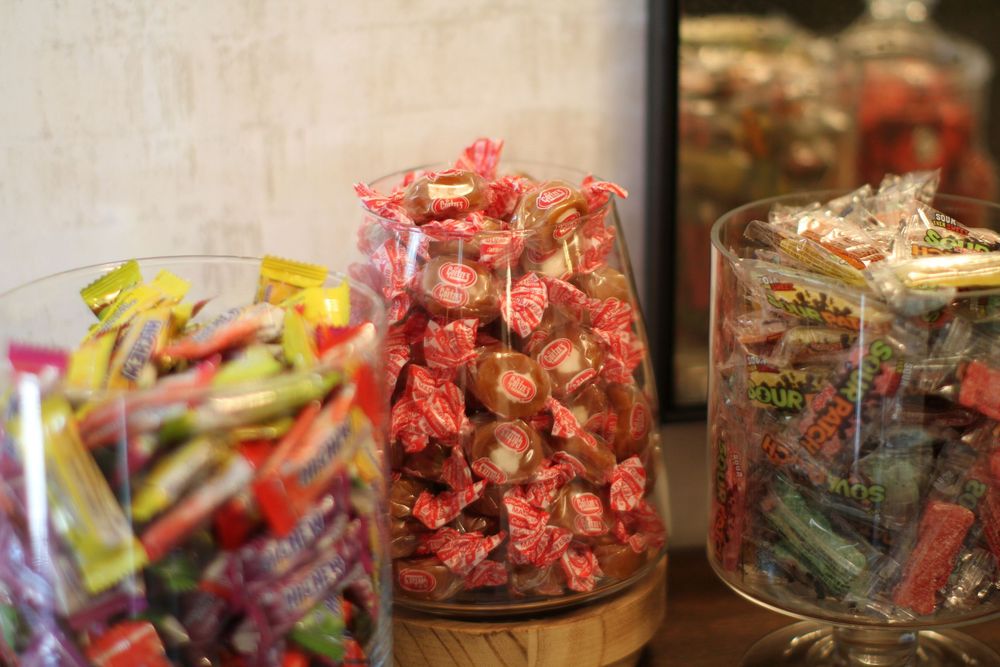 Glass jars filled with colorful wrapped candies arranged on a wooden surface in a retail display.