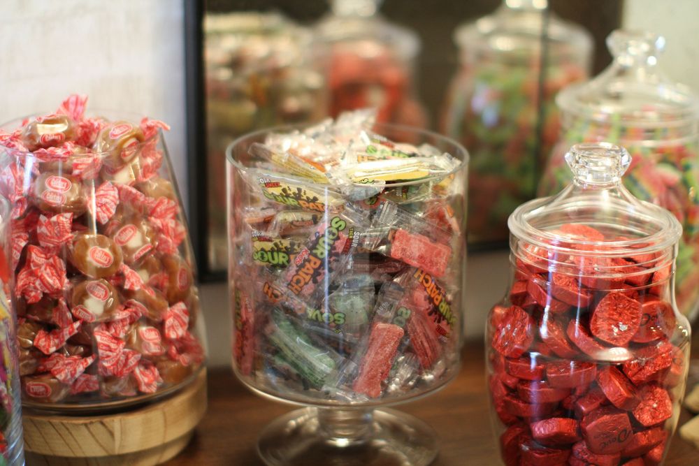 Glass jars filled with wrapped candies and sweets in red and white colors displayed on a counter.