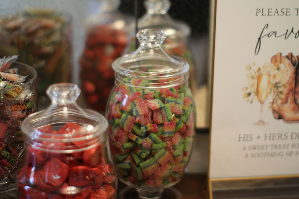 Glass canning jars filled with colorful preserved fruits and vegetables sit in a row on a wooden surface.