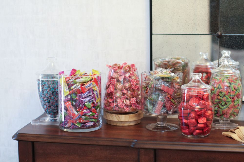 Glass jars filled with colorful candies and sweets arranged on a wooden table display.