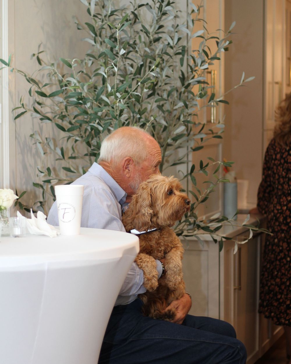 Person cuddles with a golden brown teddy bear while sitting in a white bathtub.