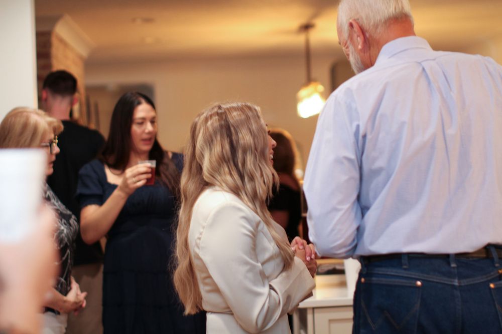 Guests enjoy drinks and conversation at a social gathering in a brightly lit room.