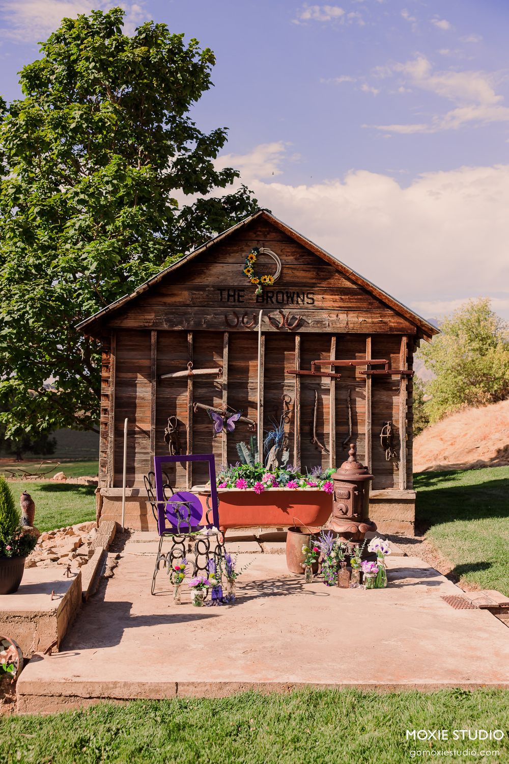 Rustic wooden cabin with wide porch and columns sits against blue sky and green trees.