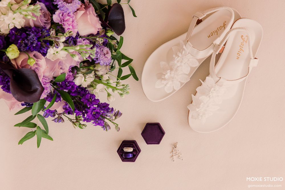 White ballet shoes and purple flowers arranged on pink background.