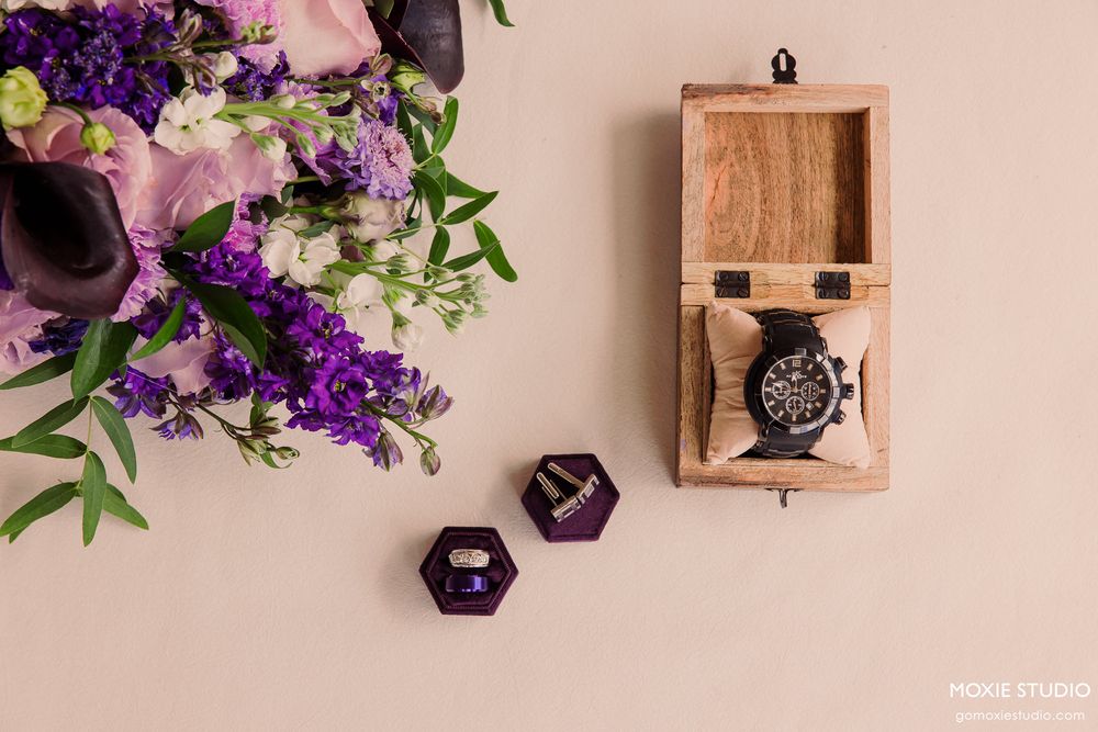 Wedding rings displayed in wooden box with purple flowers.
