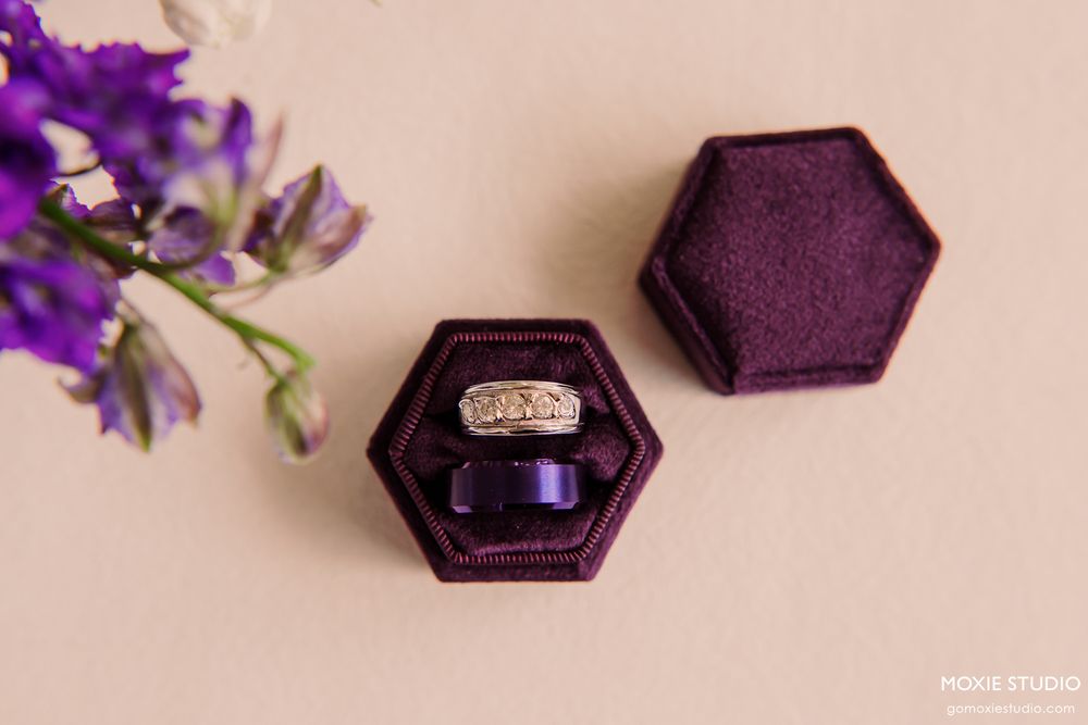 Purple hexagonal ring boxes arranged with flowers on beige surface.