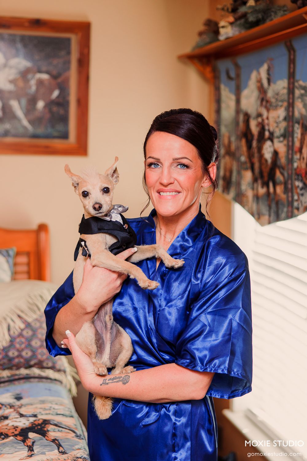 Person in blue satin robe holds small chihuahua during wedding morning preparations.