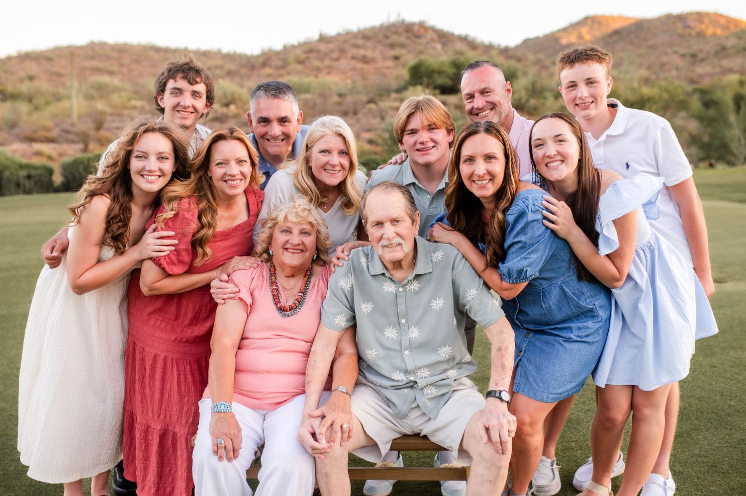 Large multigenerational family posing together on a green lawn at a warm sunset.