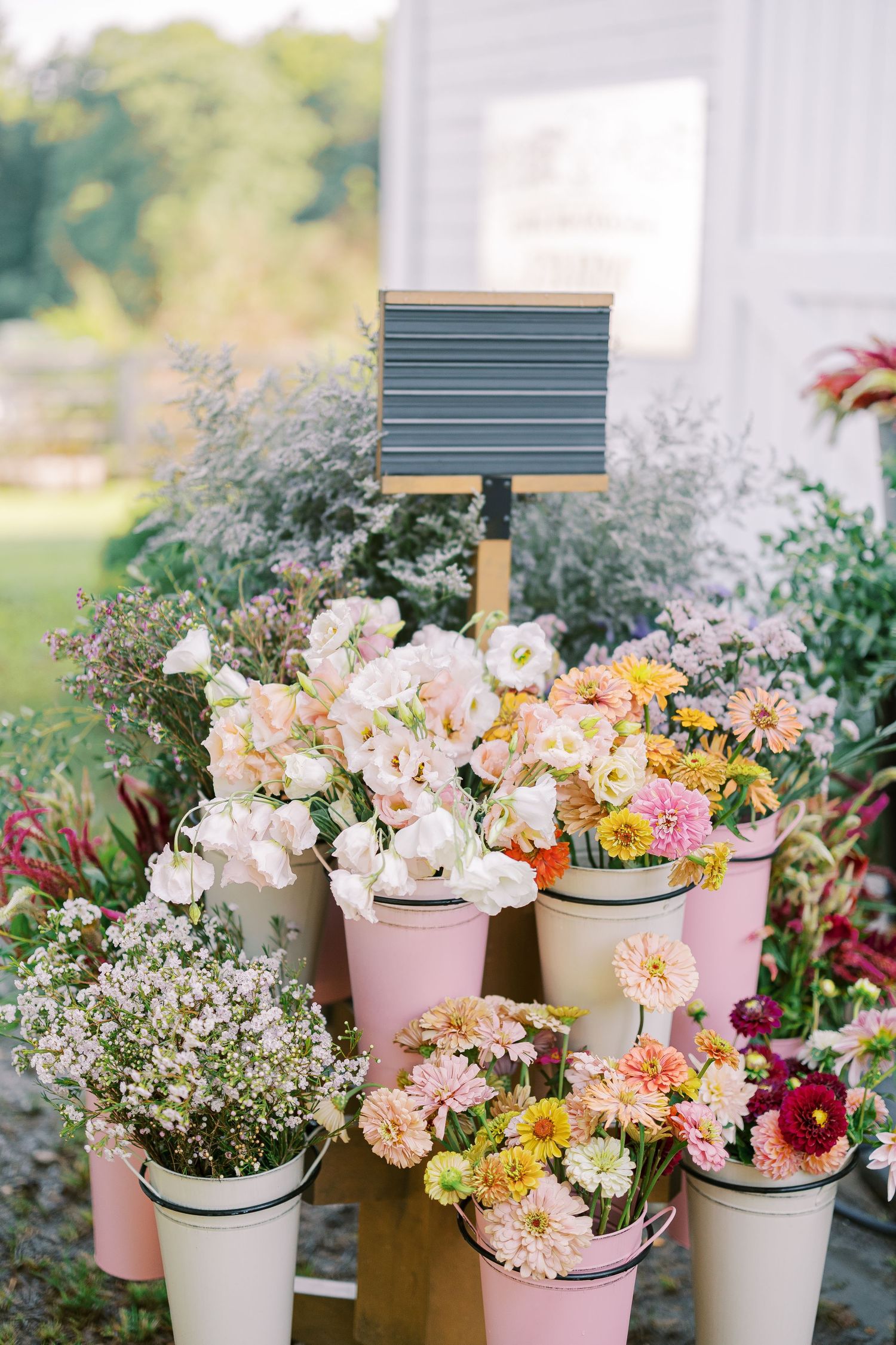 Garden-style flower display with pink and white blooms in pastel buckets with price signage.