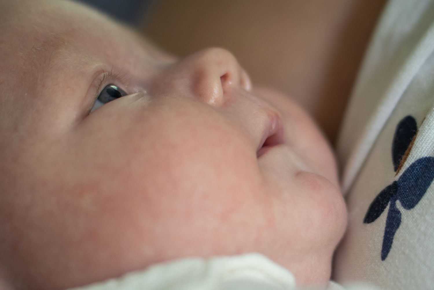 Close-up of a peaceful newborn baby with soft skin and bright eyes, gently cradled during a feeding moment.