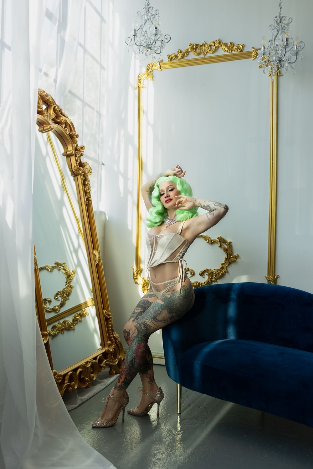 Artistic portrait in luxurious setting with ornate gold mirrors, blue velvet couch, and model with mint green hair.