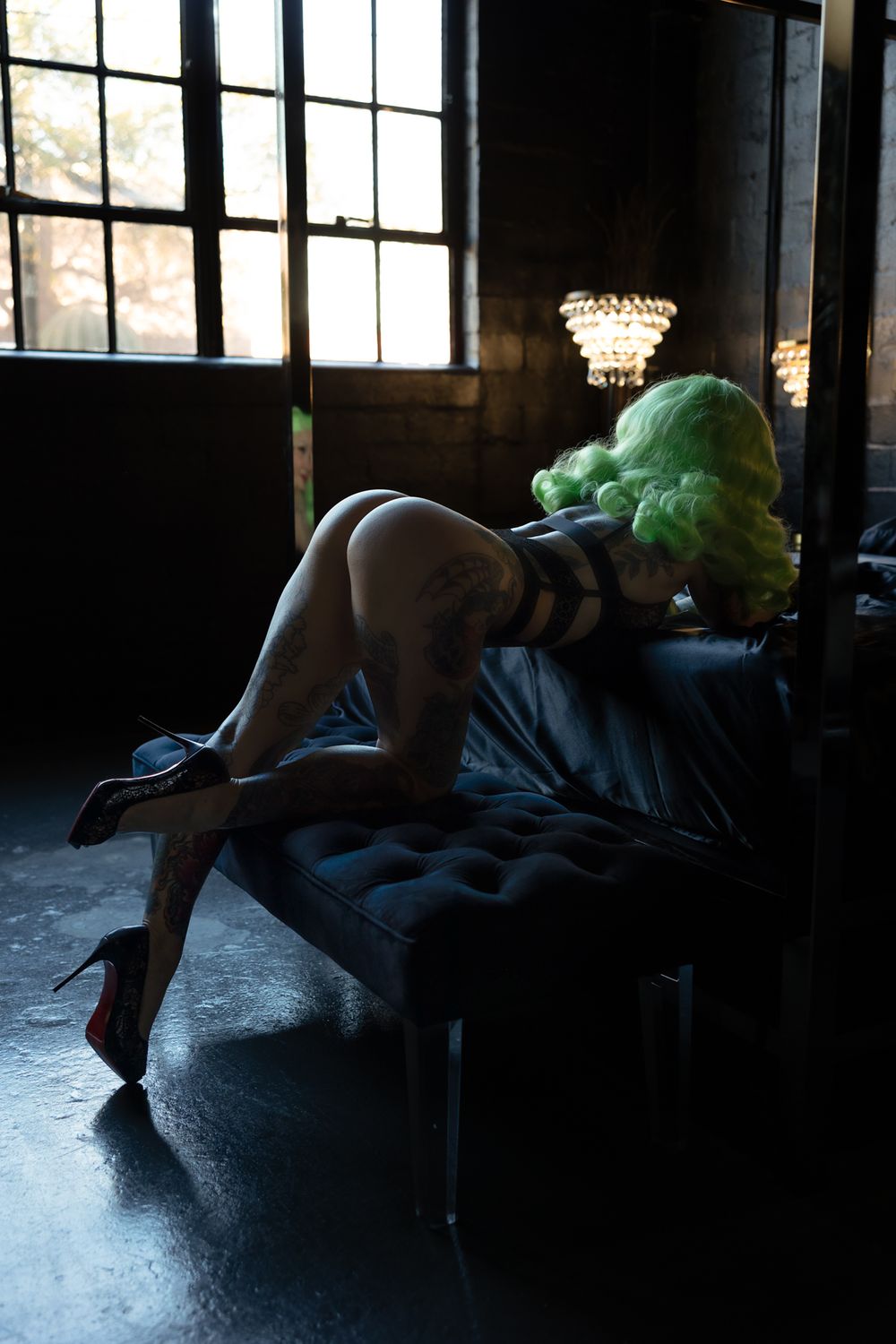 A figure in dark clothing lies on a floor in a moody, dimly lit room with windows creating dramatic shadows.