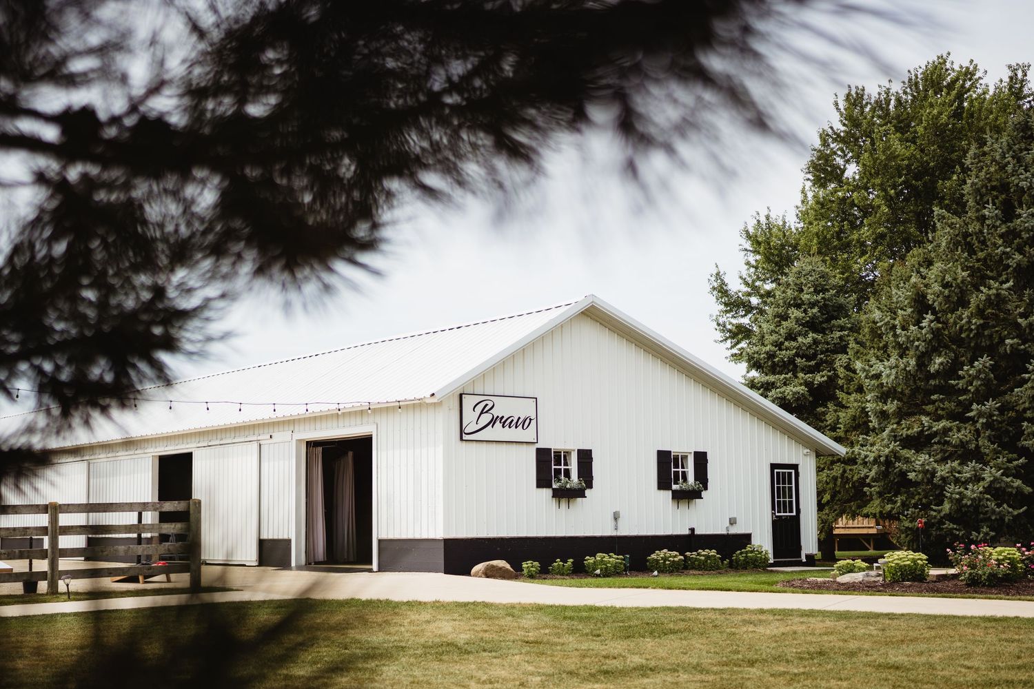 Long white barn buildings with black trim stand in a row against a cloudy sky and green trees.