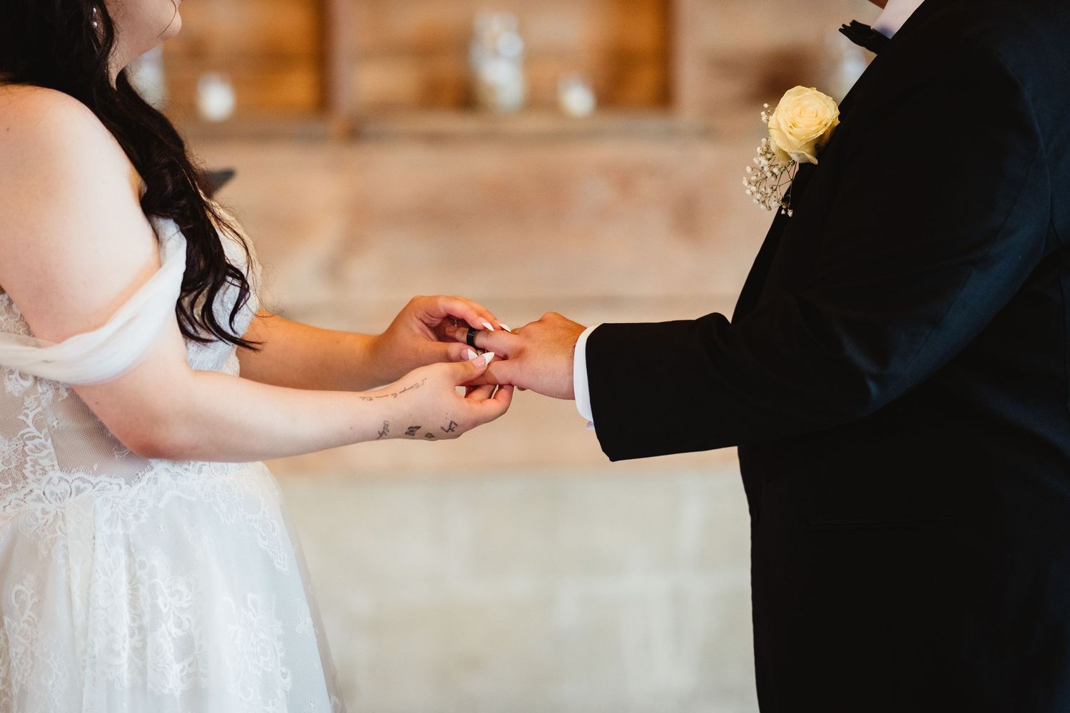 Close-up of hands during wedding ring exchange ceremony with bride wearing white lace dress.