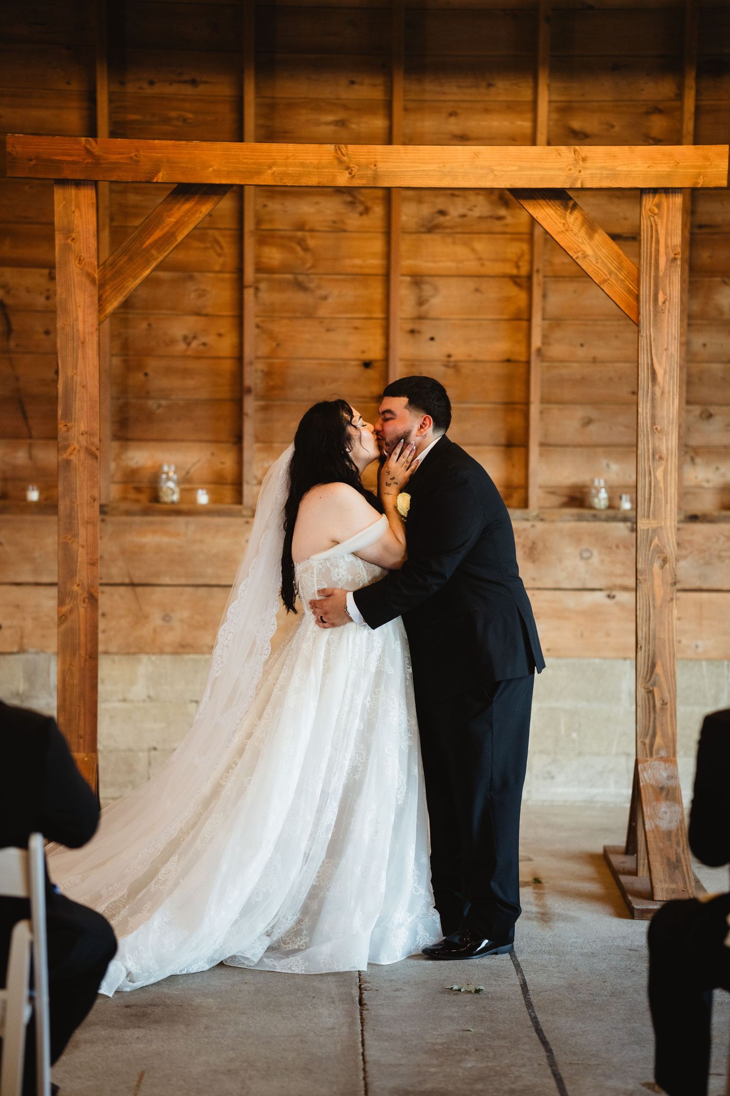 Romantic newlyweds share a tender moment inside a rustic wooden barn decorated with candles.