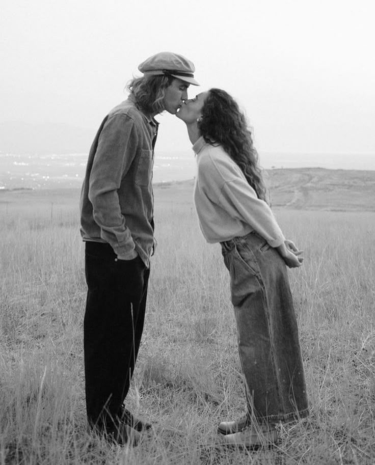 A black and white photo series shows a couple standing close together in an open field having a conversation.