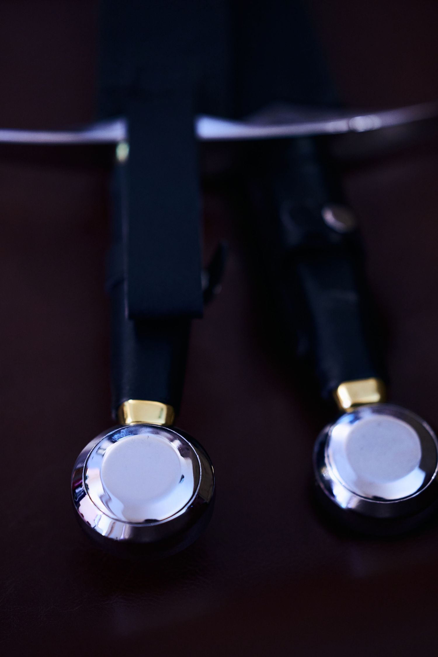 Close-up of black earbuds with silver metal accents and gold trim details on a dark background.