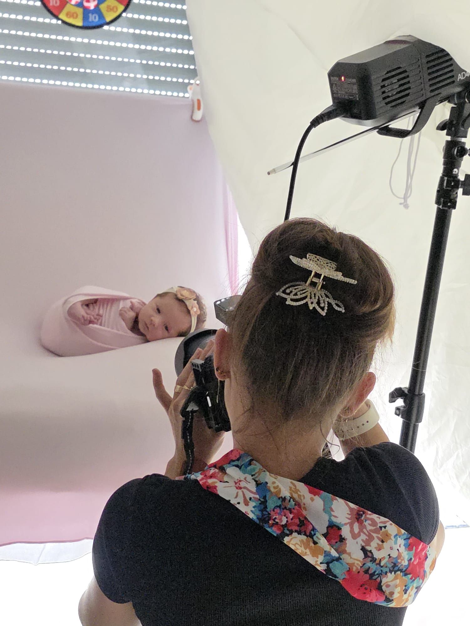 Behind-the-scenes photo of professional photographer capturing newborn portraits in a pink studio setup.
