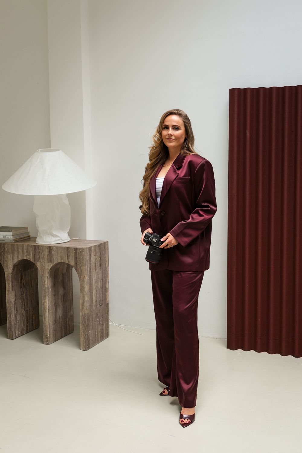 Burgundy velvet power suit with matching pants and high heels styled with a white lamp and wooden side table.