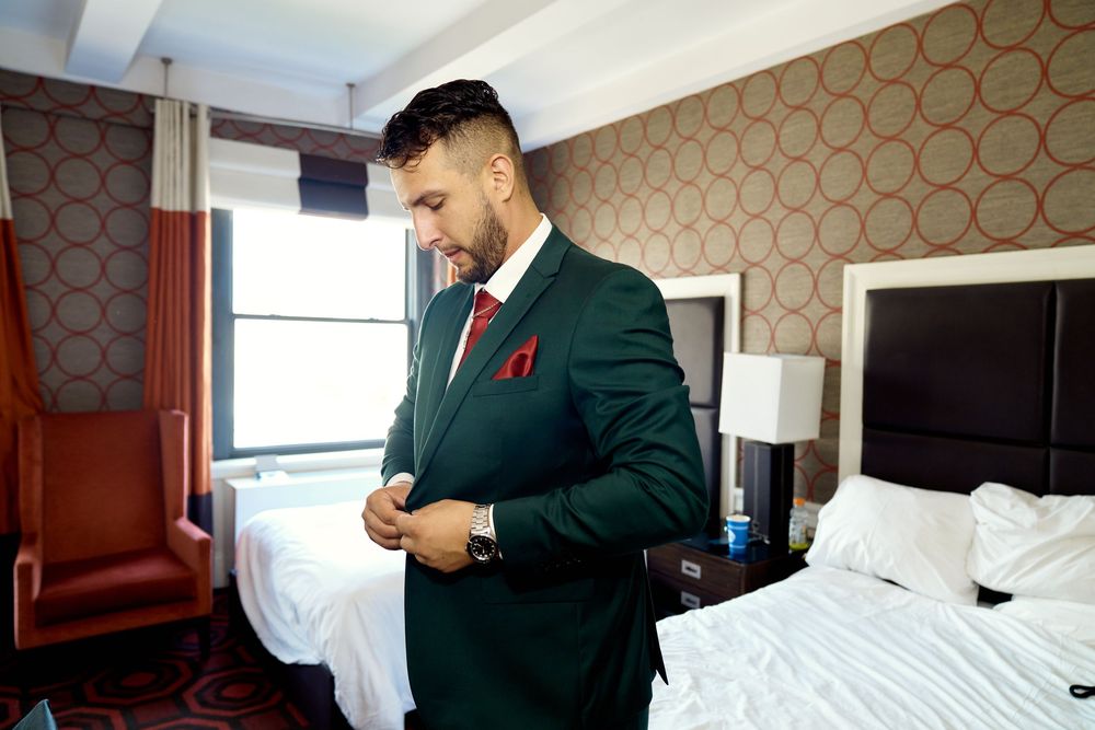 Hotel staff making bed with crisp white linens in modern room with patterned wallpaper.