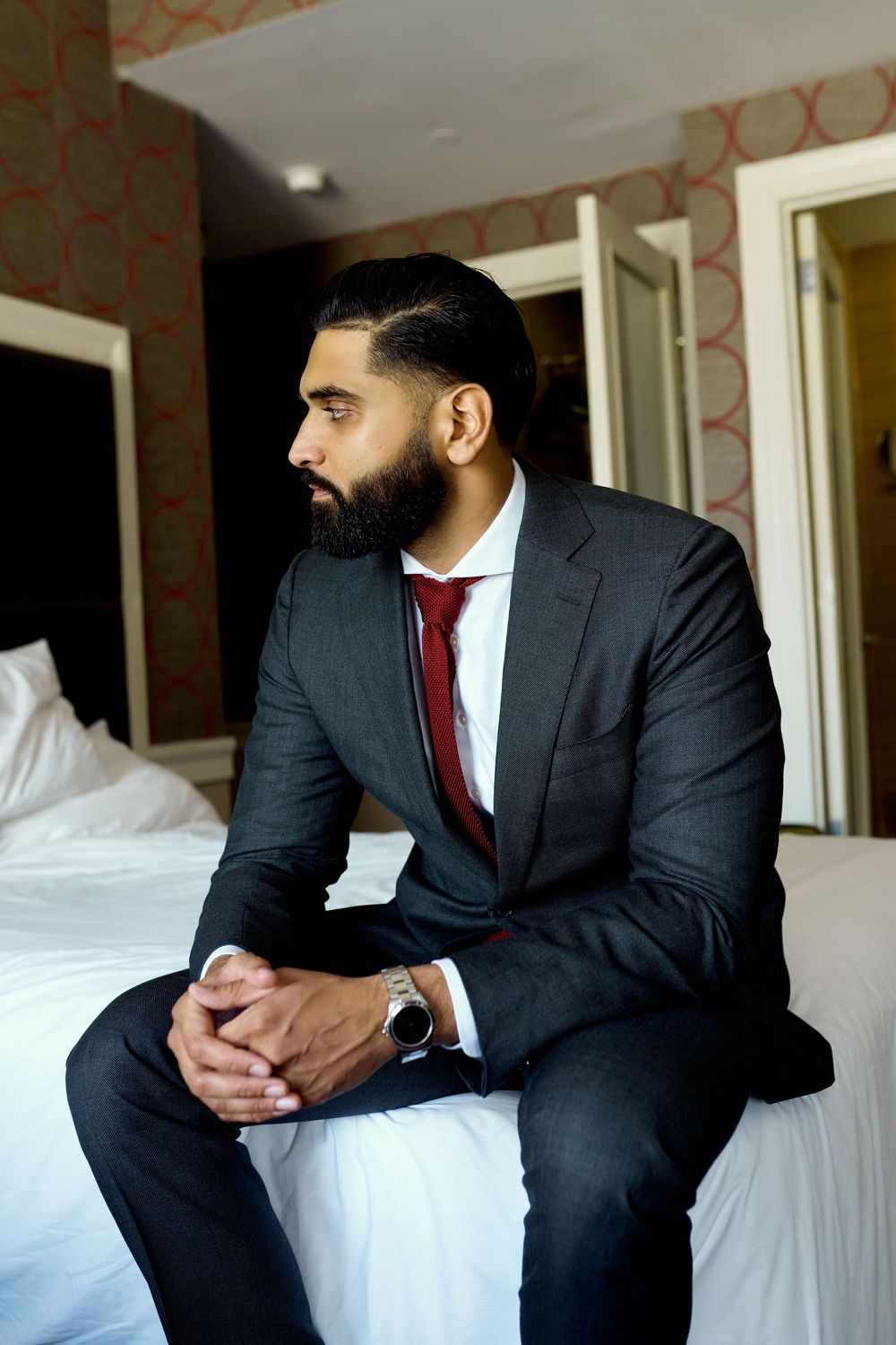 Professional in dark suit and red tie sits contemplatively on white hotel bed in series of connected poses.