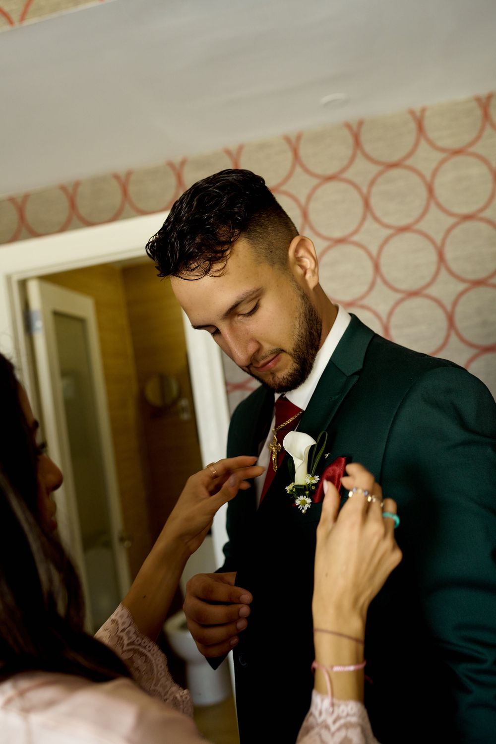 A boutonniere is pinned onto an elegant green suit jacket during a formal event preparation.