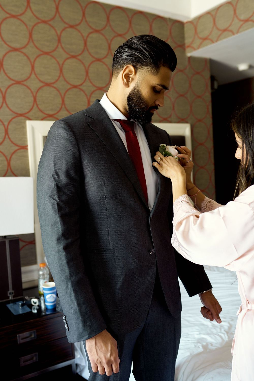 A person adjusts a red tie while wearing a dark business suit in what appears to be a hotel room.