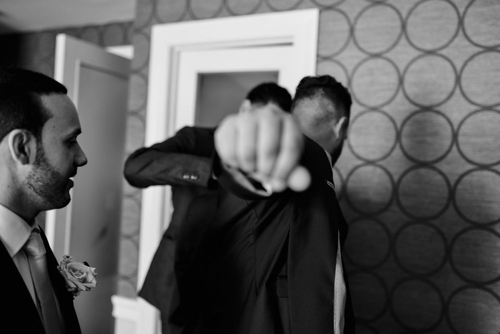 Black and white candid moment of groomsmen getting ready before a wedding ceremony.