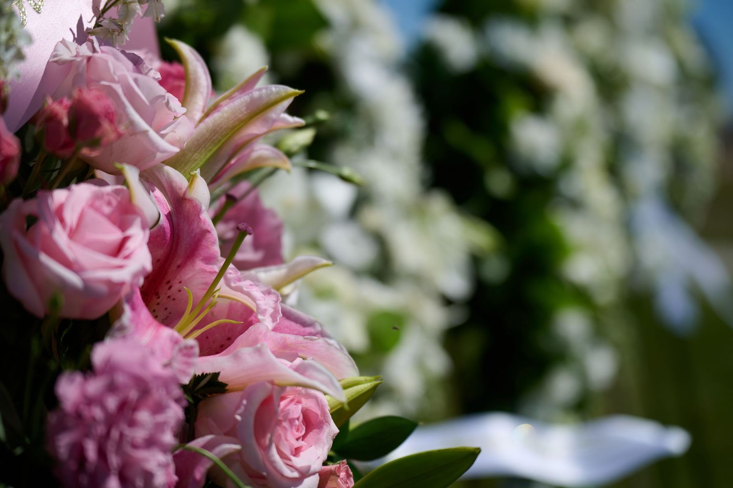 Beautiful pink roses and lilies in a floral arrangement with soft white bokeh background blur.