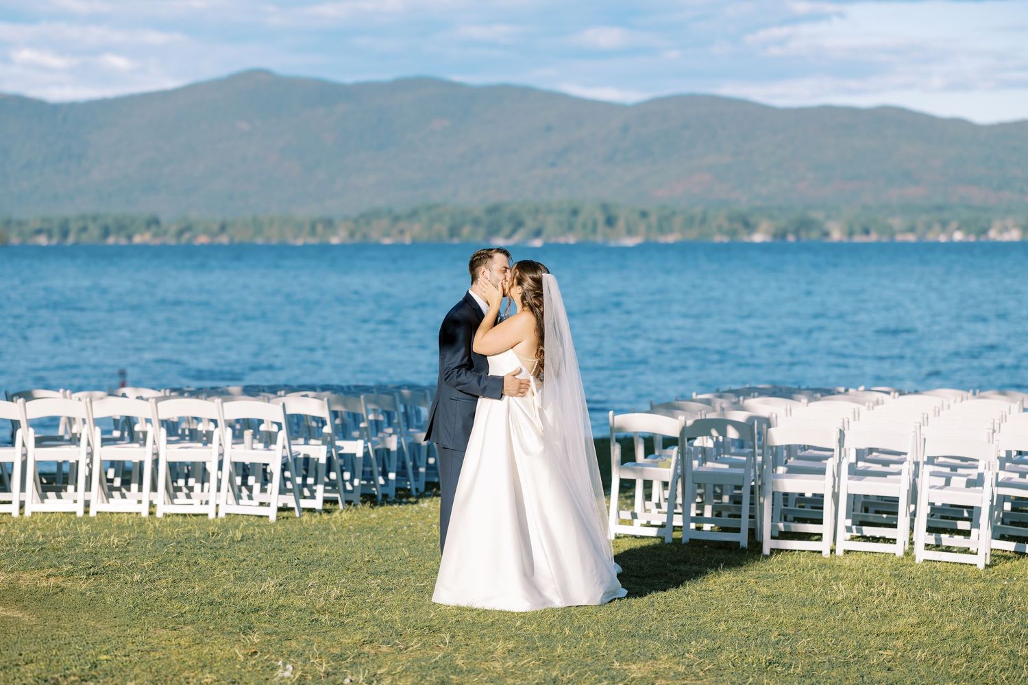 Wedding ceremony setup overlooking a scenic mountain lake with white chairs arranged on a grassy hilltop.
