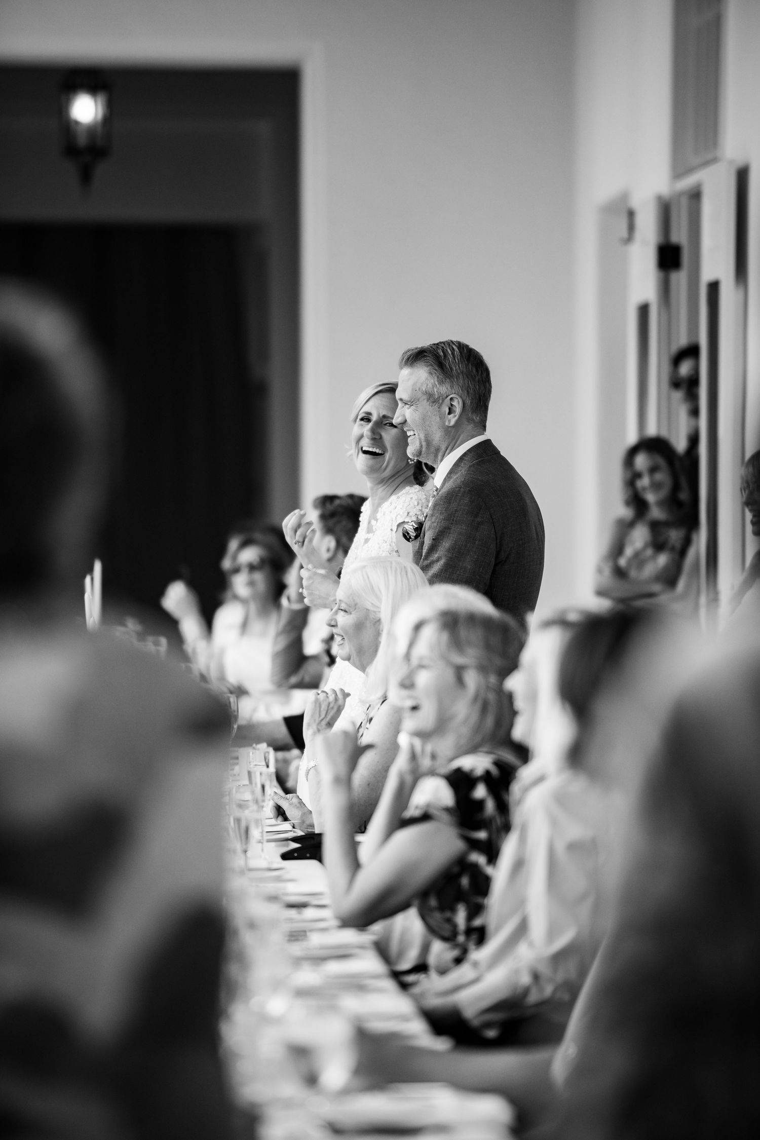Wedding reception guests seated at long tables during speeches and toasts in black and white.