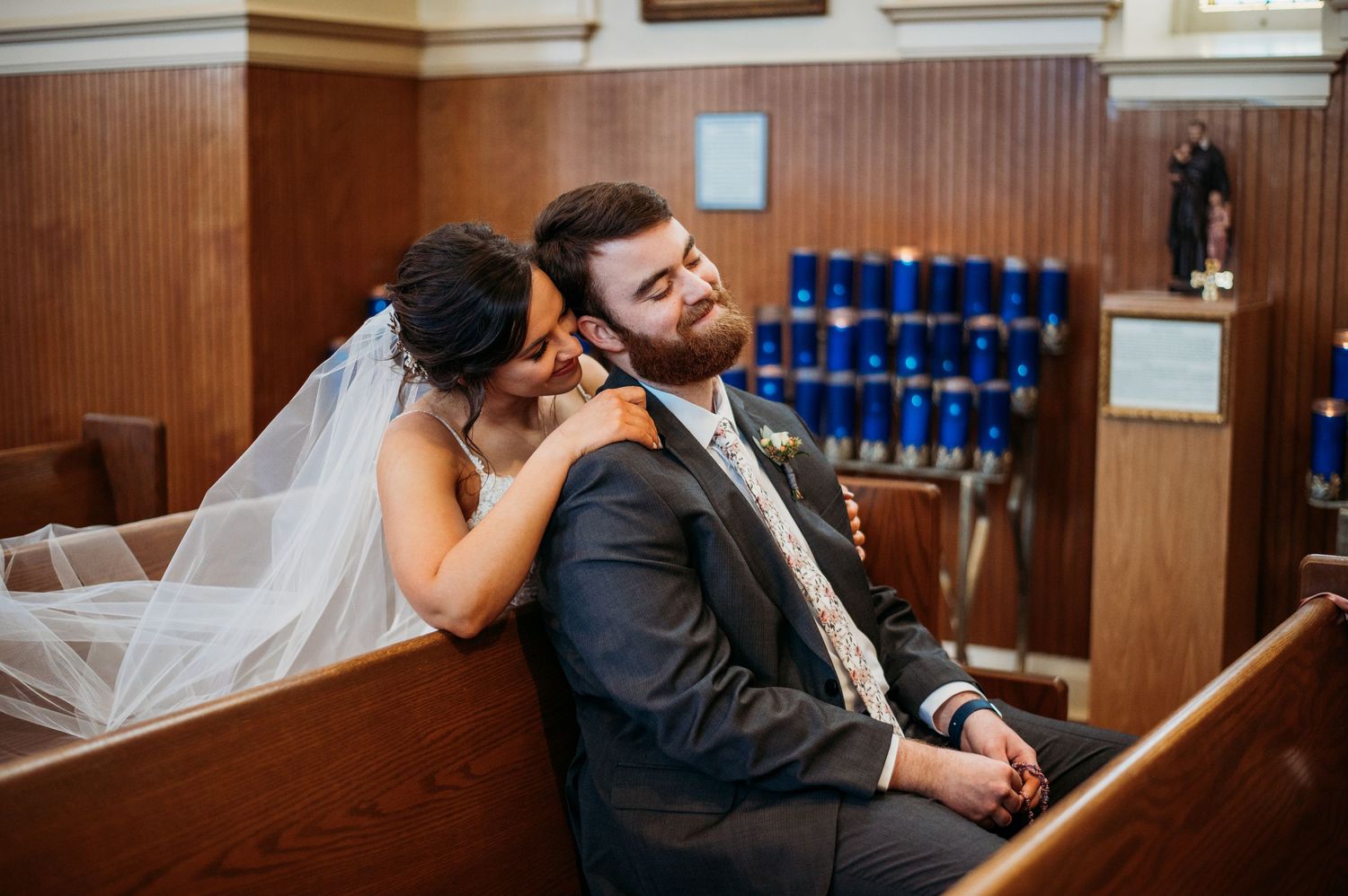 A couple shares a playful moment in a church pew beneath a decorative stained glass window.