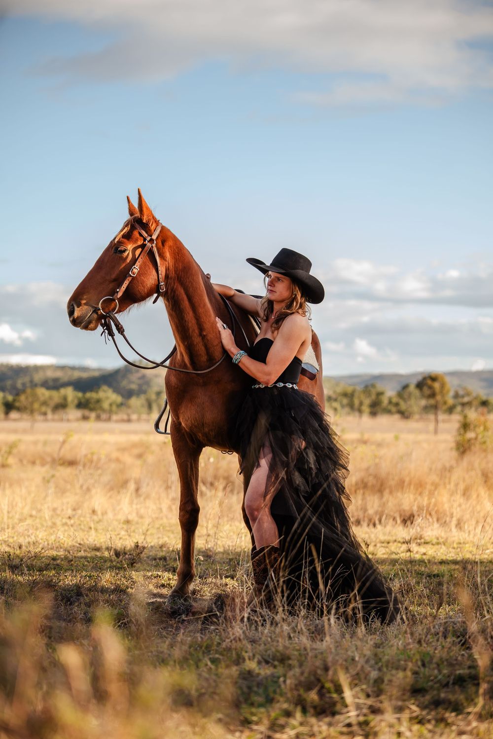 Chestnut horse and rider in black attire enjoying a scenic countryside landscape at sunset.