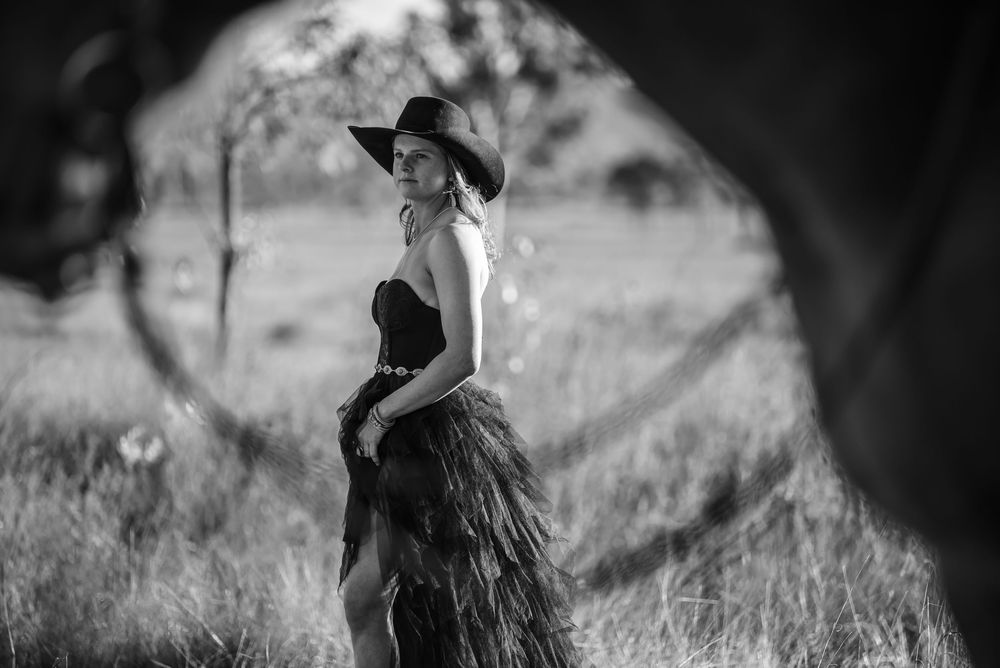 Silhouetted equestrian wearing a cowboy hat poses with horse against dramatic black and white background.