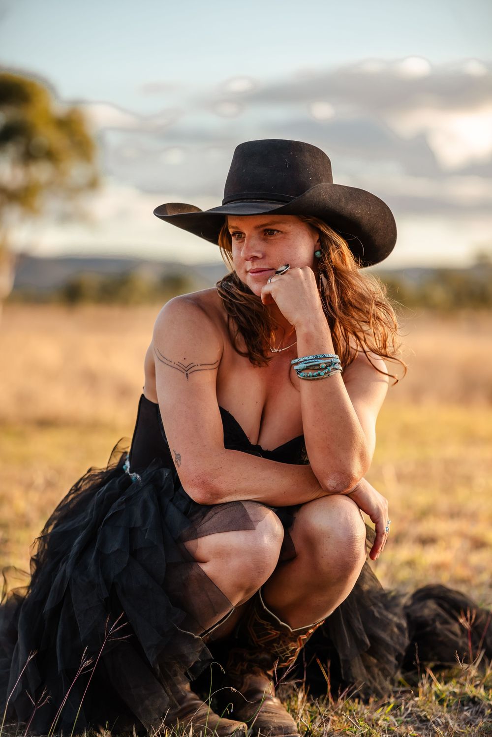 A person wearing a cowboy hat relaxes in a rustic field with dramatic clouds during golden hour.