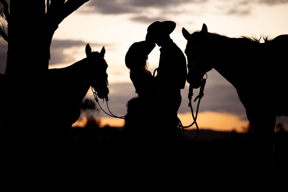 Silhouettes of horses and riders against a dramatic sunset sky create a western panorama.