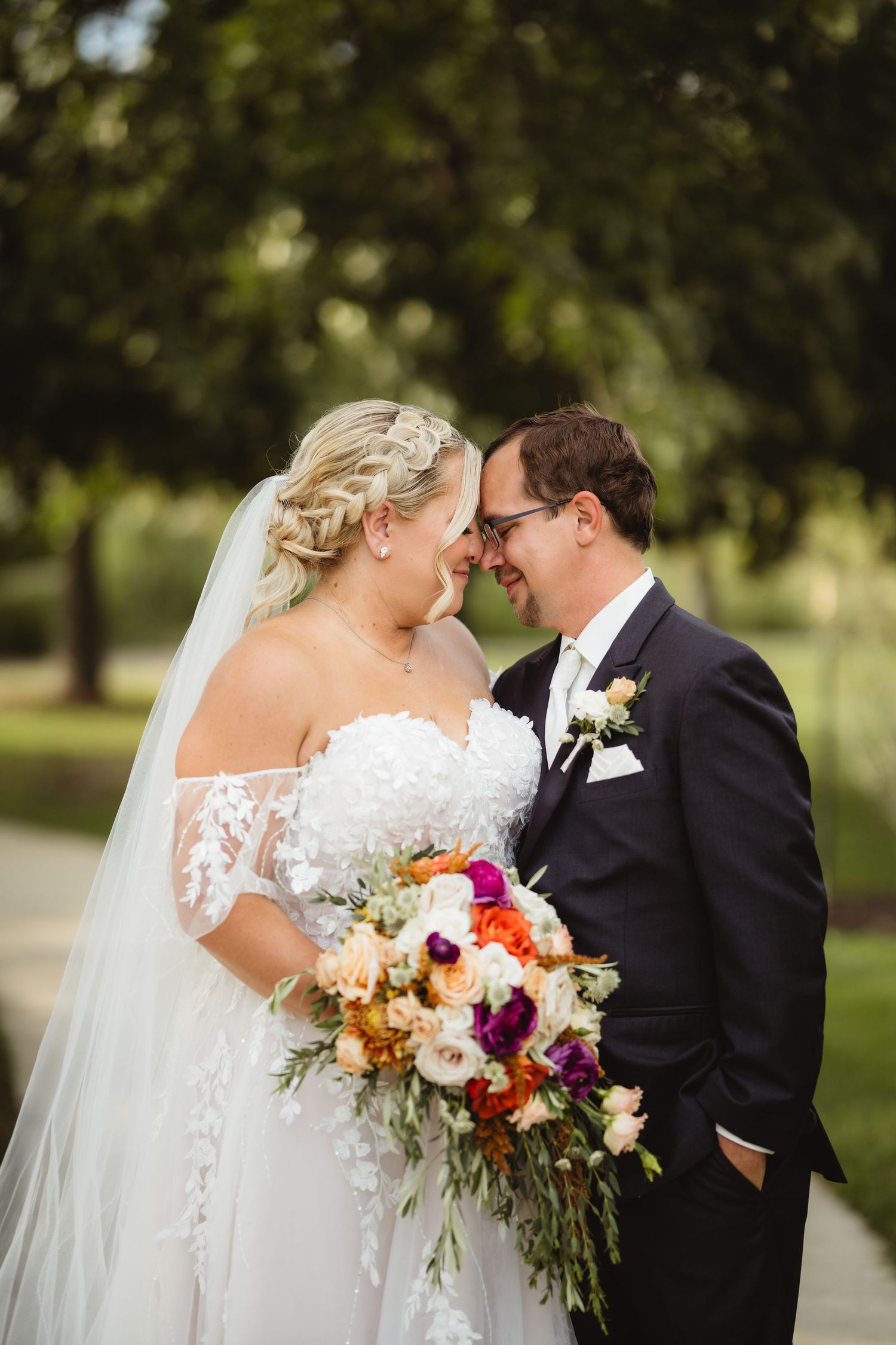 Bride and groom share romantic moments outdoors with vibrant fall-colored wedding bouquet featuring purple and orange blooms.
